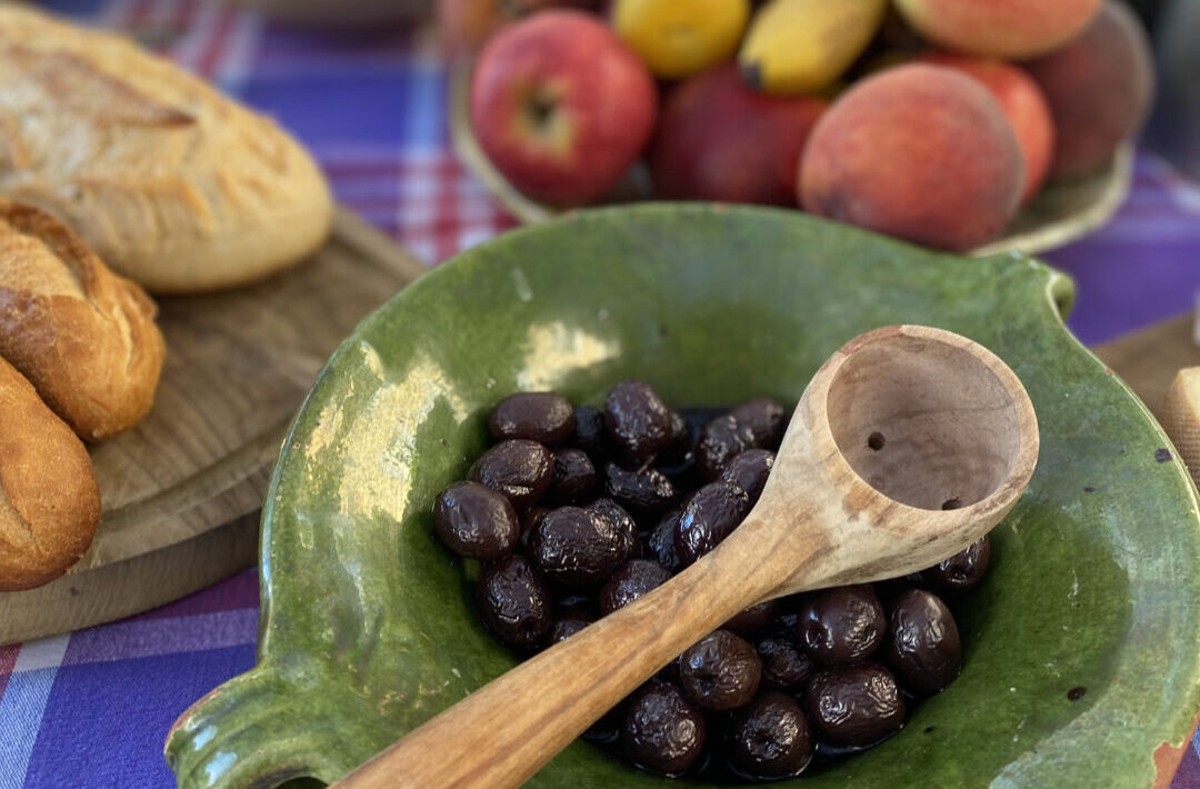 bowl of black olives, mixed fruit and a board with bread