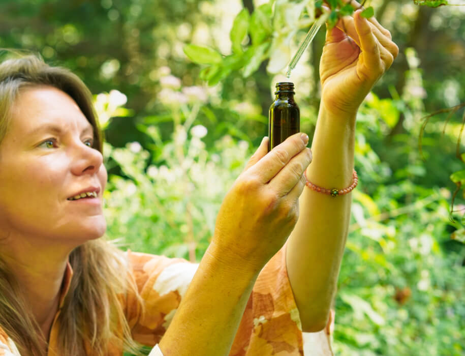 Untitled Blonde woman holding an open bottle of flower essence towards the sunlight