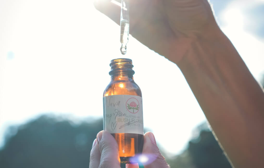 Small brown glass bottle of flower essence held up to the sunlight