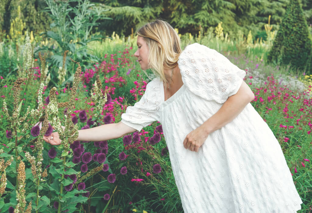 Blonde woman in a white dress reaching out to touch flowers